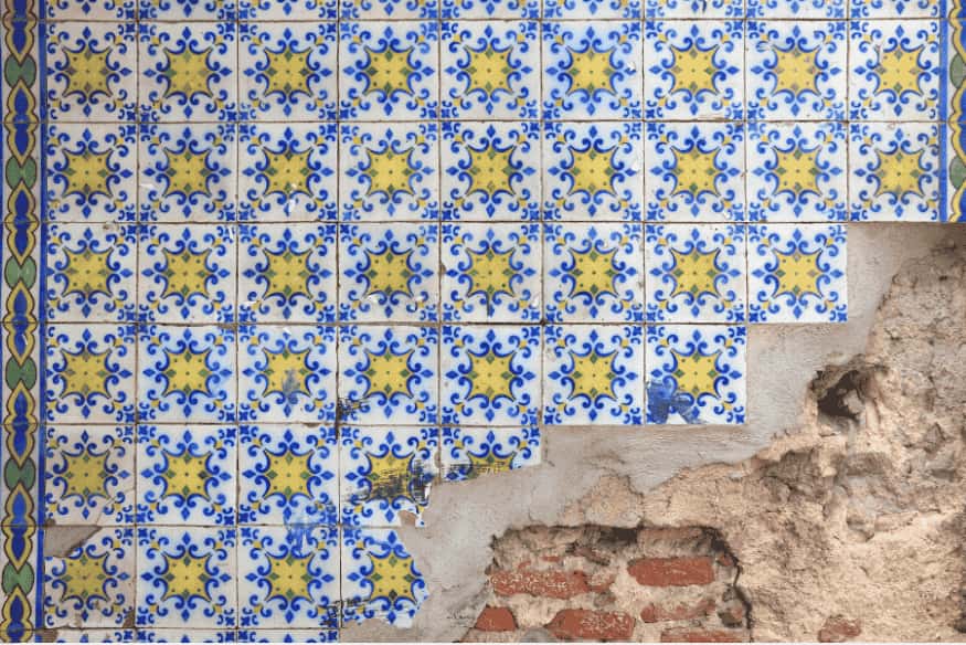Parede com azulejos antigos azul e amarelo danificados e reboco exposto.