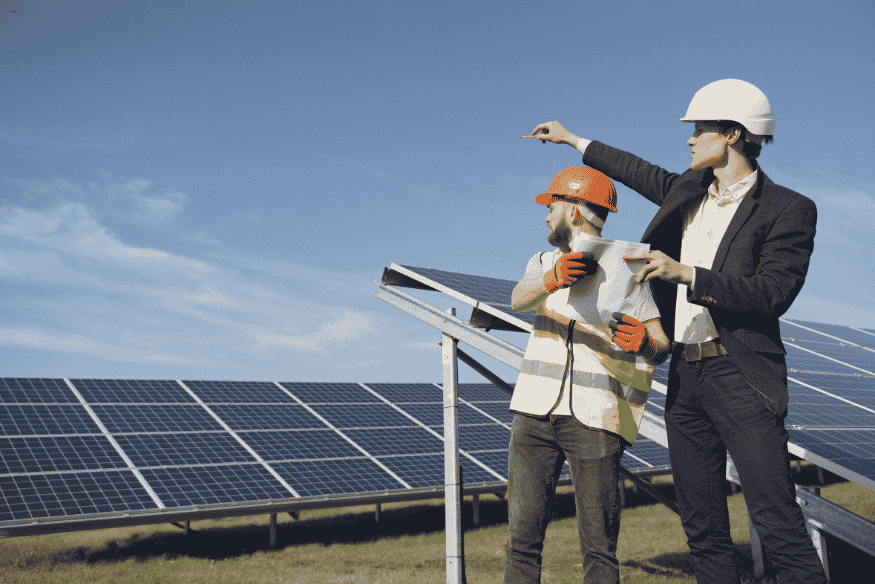 Dois engenheiros analisando projeto em frente a painéis solares em campo aberto.