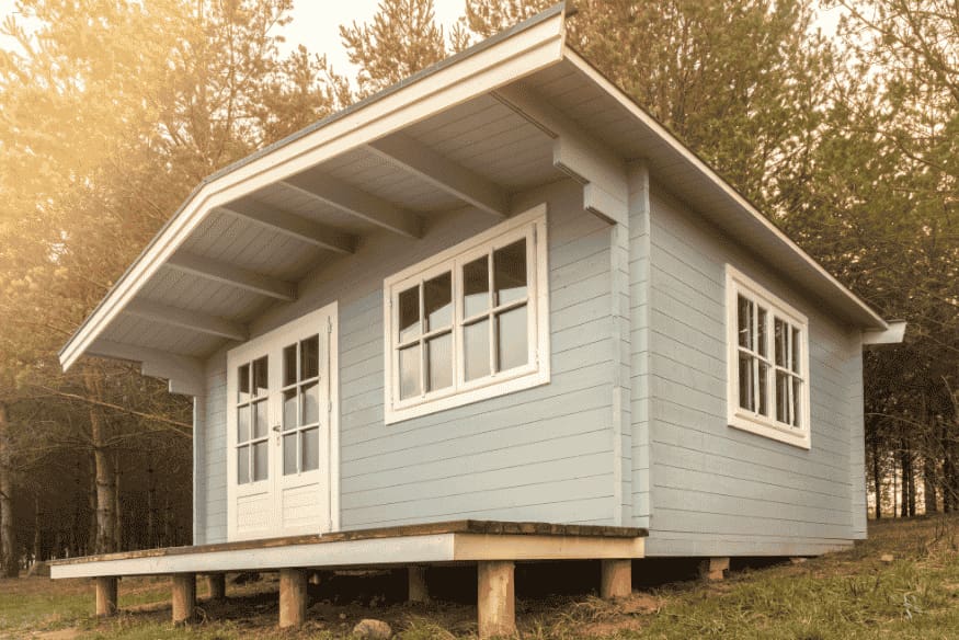 Casa de madeira elevada em terreno arborizado, projetada para eficiência energética.