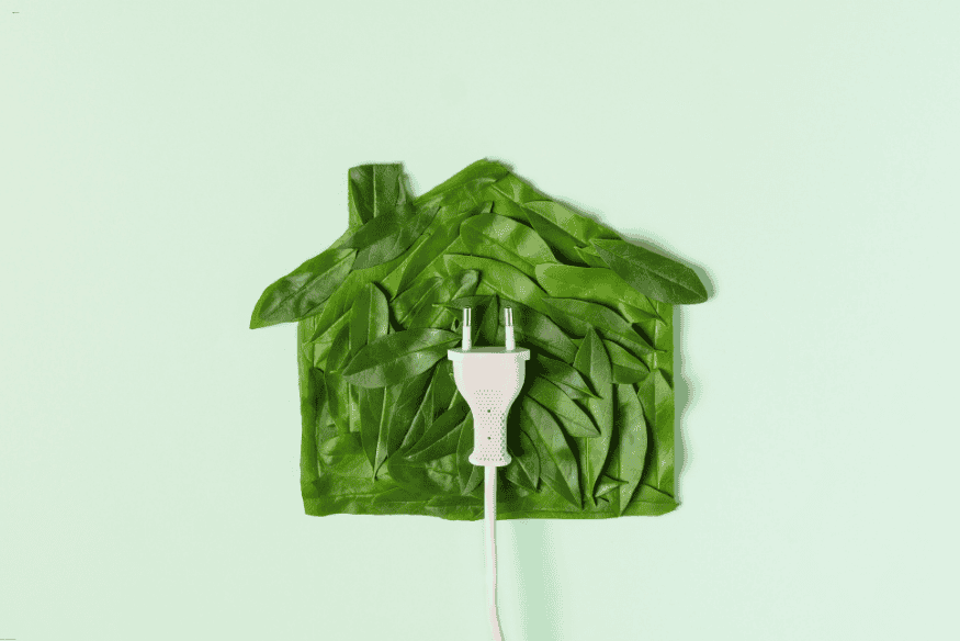 Ilustração de casa feita de folhas verdes com tomada elétrica conectada.