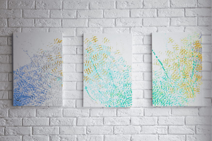 Trio de quadros abstratos com tons de azul, verde e dourado em parede de tijolos brancos para decoração moderna