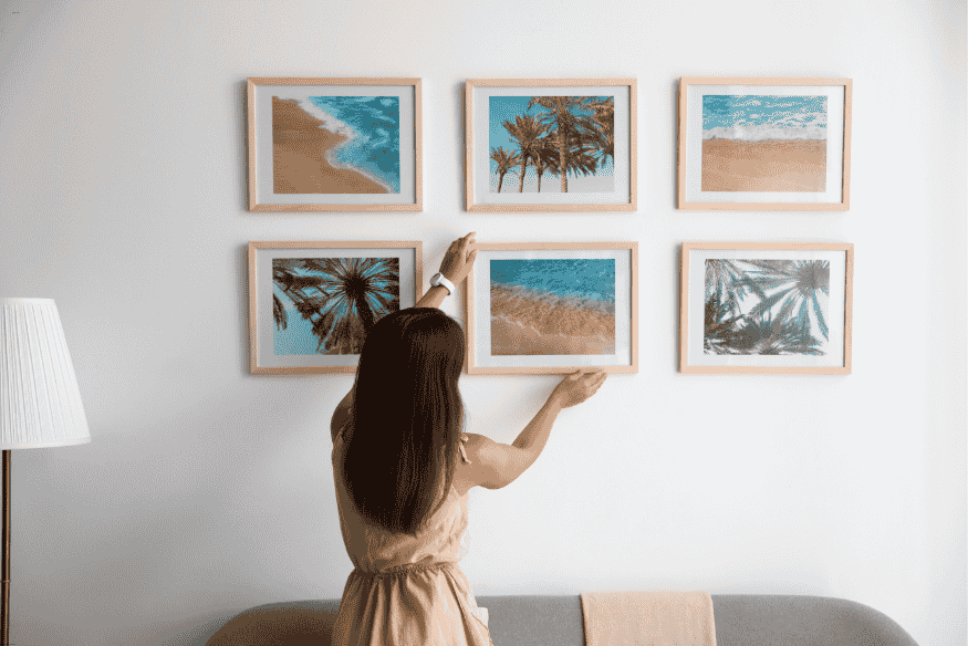 Mulher posicionando quadro com paisagem de praia e coqueiros em composição de seis molduras na parede
