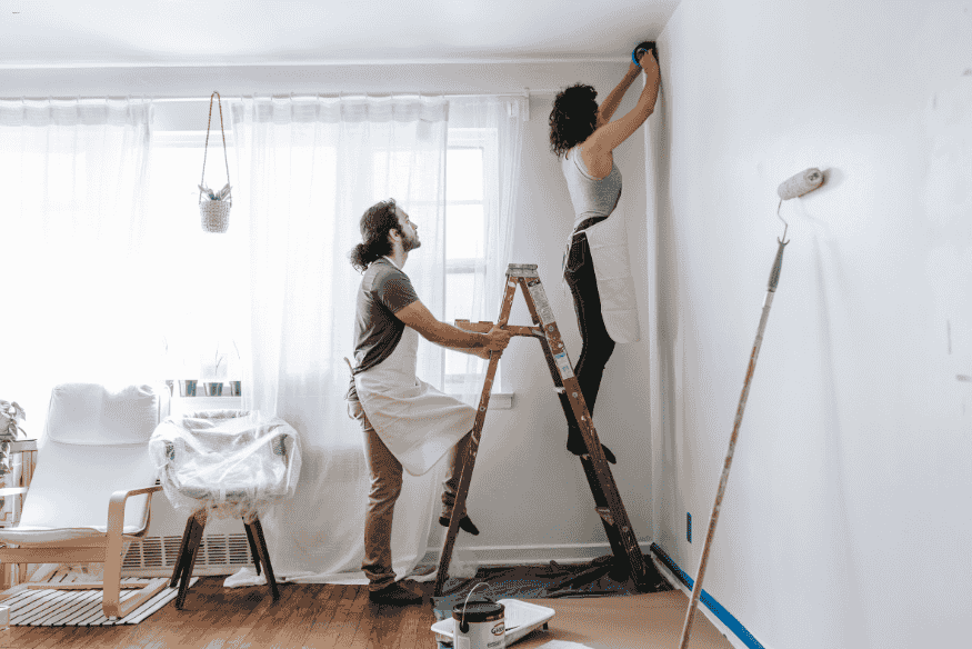 Casal pintando parede branca durante reforma caseira.