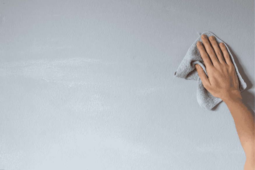 Mão limpando a parede com pano para preparar a superfície antes de aplicar papel de parede.