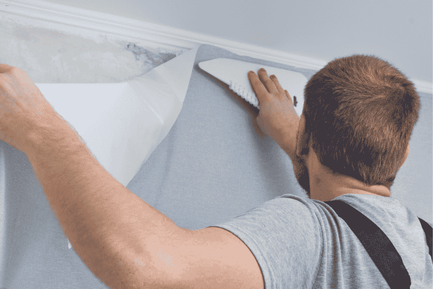 Homem aplicando papel de parede com espátula para alisar a superfície.