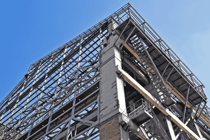 Estrutura metálica de grande porte em construção contra o céu azul.