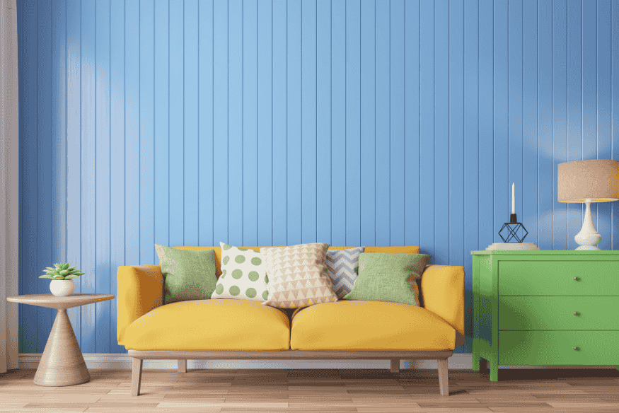 Sala com sofá amarelo, parede azul e decoração verde vibrante, tendência ousada para 2025.