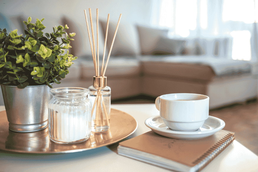 Bandeja decorativa com vela, aromatizador, planta e xícara de café em sala de estilo escandinavo.