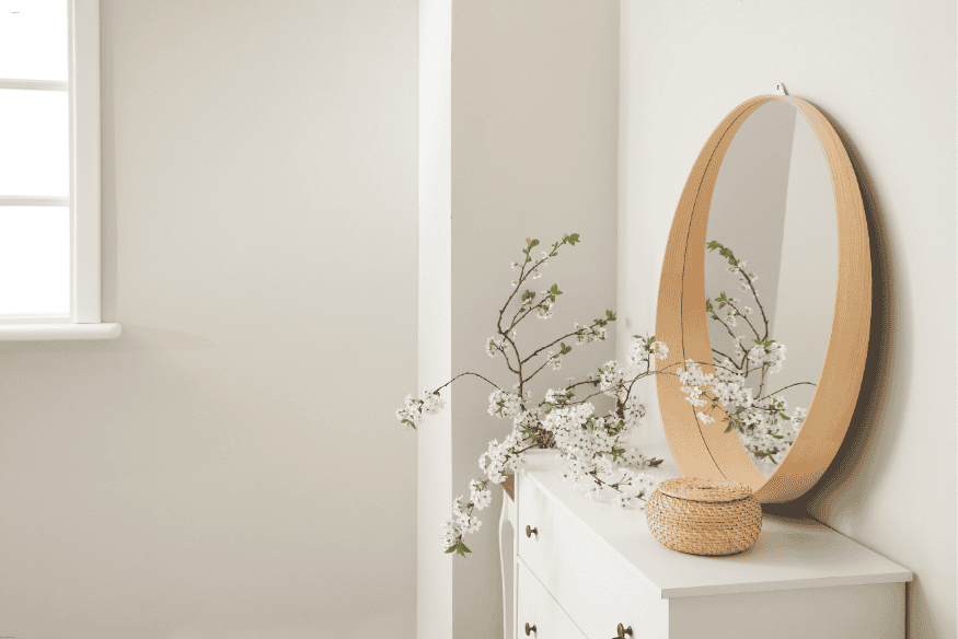 Cômoda minimalista com espelho redondo e galhos floridos em decoração boho personalizada.