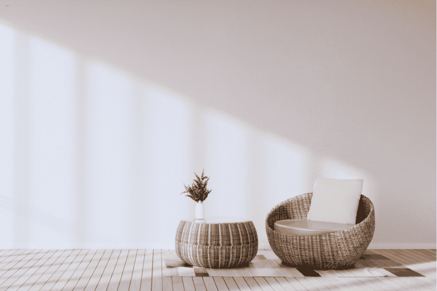 Cadeira de fibra natural com almofada branca ao lado de mesa lateral decorada com vaso.