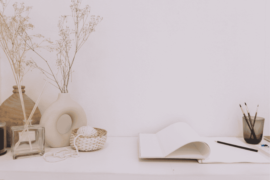 Mesa minimalista com objetos decorativos neutros, incluindo vasos de cerâmica e caderno aberto.