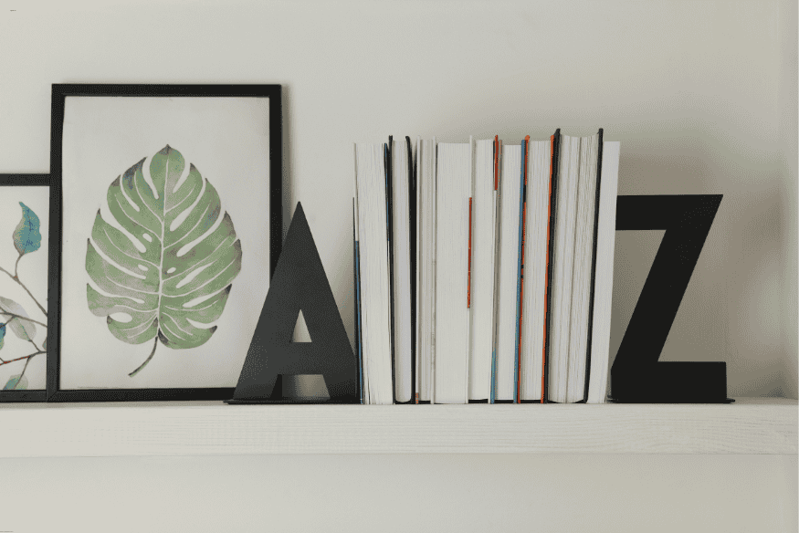 Prateleira com livros organizados e quadros de folhas verdes em molduras pretas.