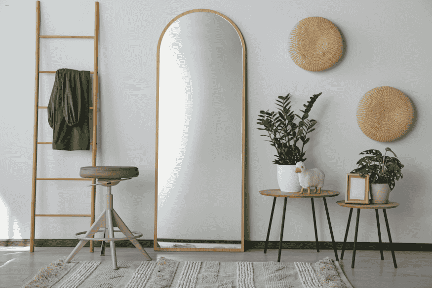 Canto decorado com espelho de corpo inteiro, plantas e elementos rústicos em sala pequena.