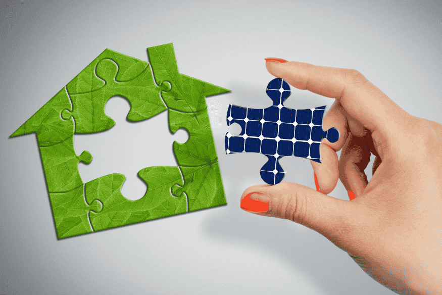 Mão encaixando peça de quebra-cabeça de painel solar em formato de casa sustentável.