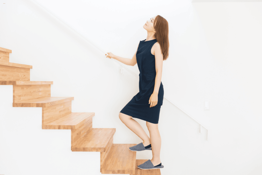 Mulher subindo escada de madeira minimalista em ambiente iluminado.