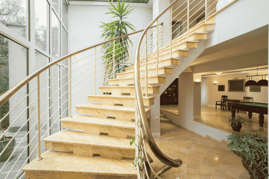 Escada interna curva de mármore com corrimão metálico em casa de luxo.