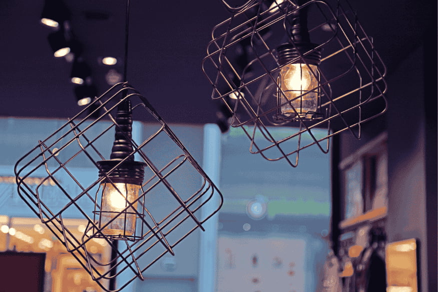 Luminárias pendentes com estrutura geométrica metálica e lâmpadas de filamento.