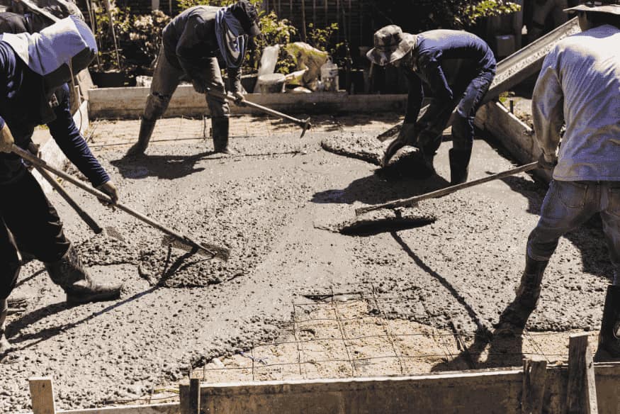 Grupo de pedreiros espalhando concreto fresco para nivelar o piso.