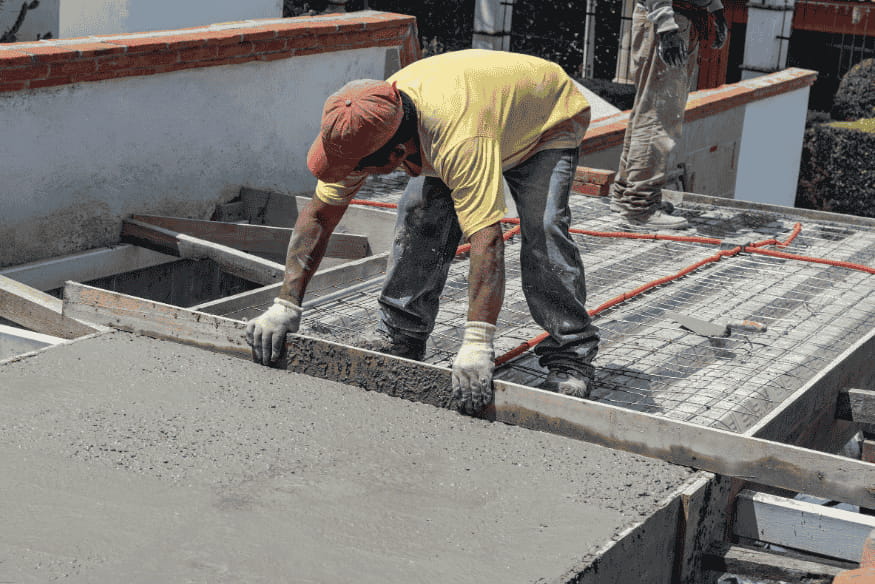 Trabalhador espalhando concreto para nivelar piso em obra residencial.