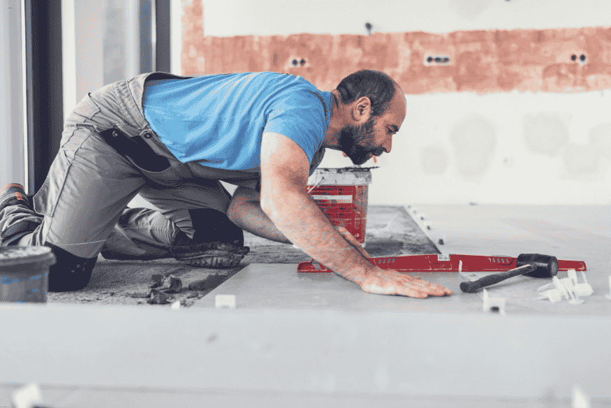Pedreiro utilizando nível e ferramentas para alinhar piso durante reforma.