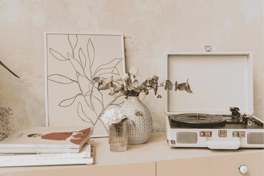Vitrola retrô portátil branca com vasos decorativos e quadro minimalista.