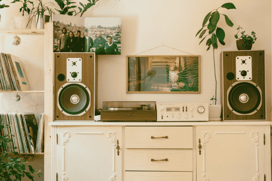 Decoração retrô com vitrola, caixas de som vintage e plantas em móvel branco.
