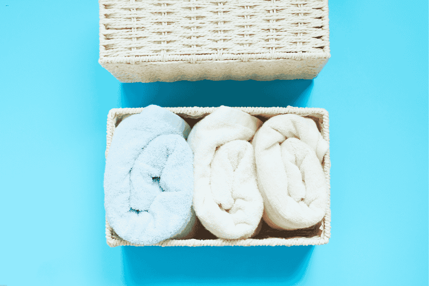 Cesto de vime com toalhas enroladas para organização decorativa.