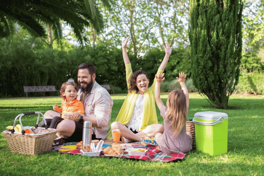 Família fazendo piquenique em área verde de jardim.