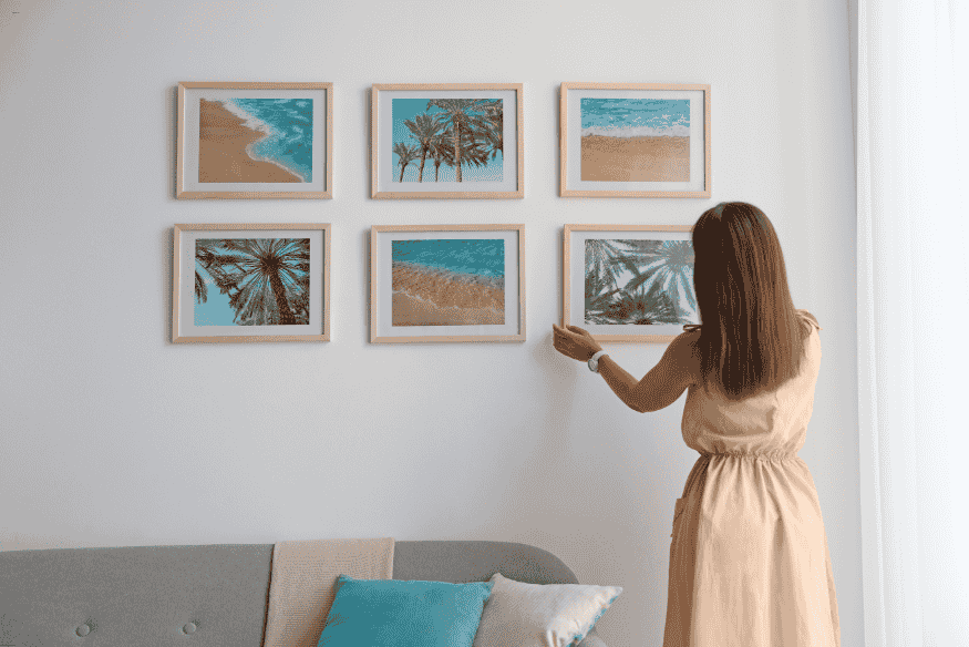 Mulher posicionando quadros de paisagens tropicais em parede branca