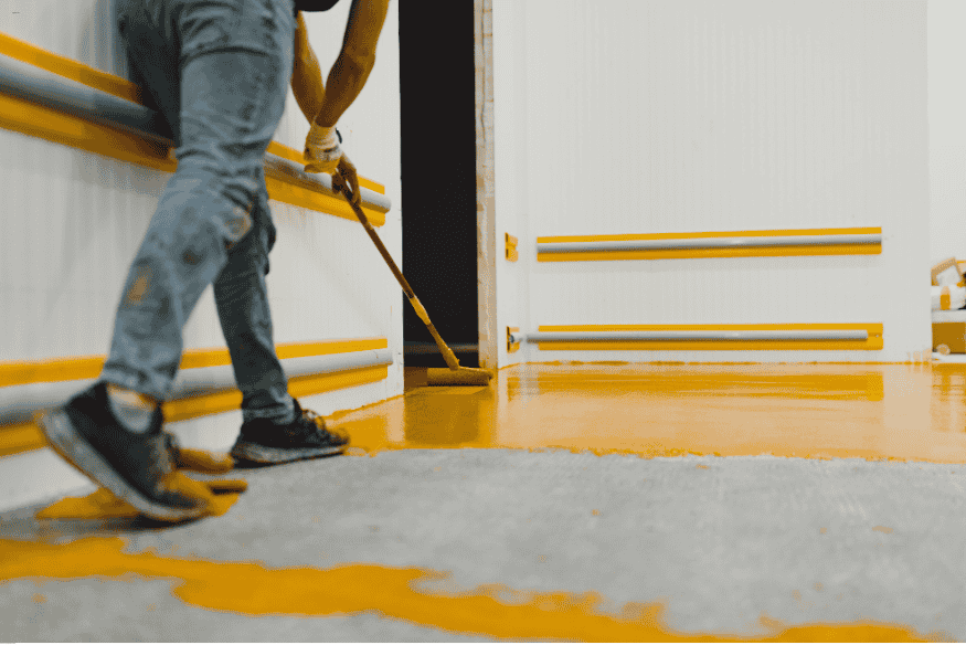 Trabalhador espalhando pintura epóxi amarela em área interna.