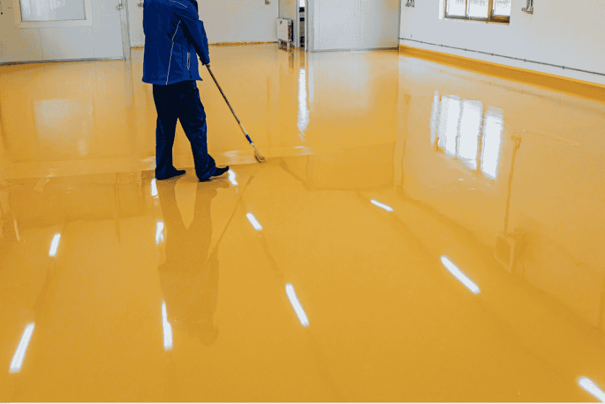 Pessoa aplicando pintura epóxi amarela em piso residencial.