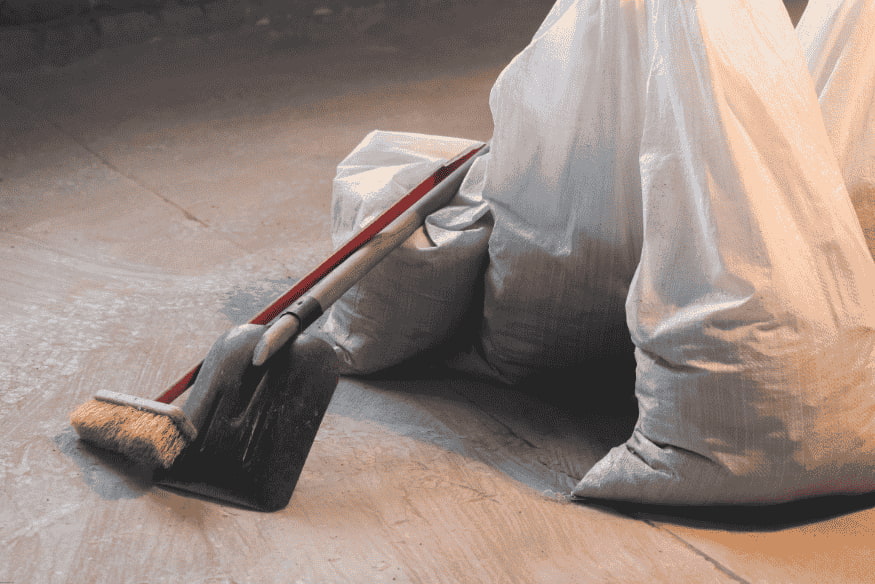 Sacos de entulho e pá de obra após limpeza no canteiro de reforma.
