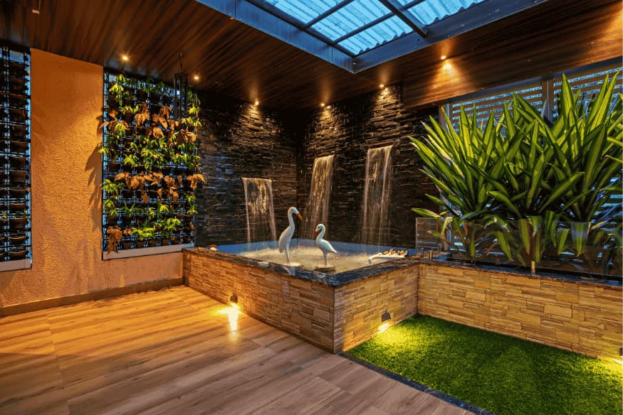 Jardim interno com parede de plantas, cascatas decorativas e esculturas de garças.