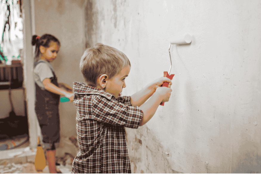 Criança ajudando a pintar parede durante reforma em casa.