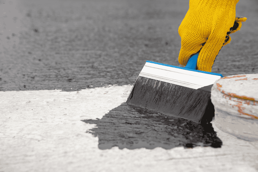 Pessoa aplicando tinta impermeabilizante preta em superfície de concreto.
