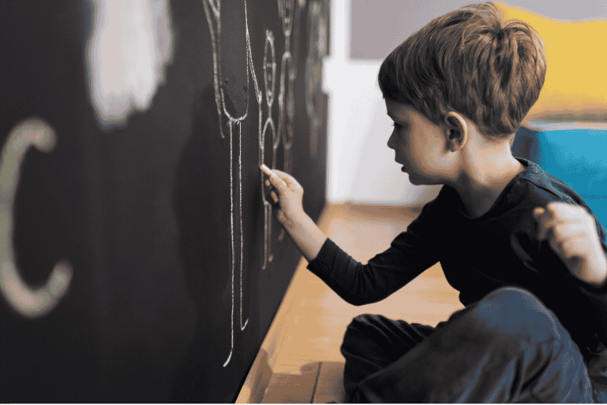 Menino desenhando em parede pintada com tinta lousa preta.