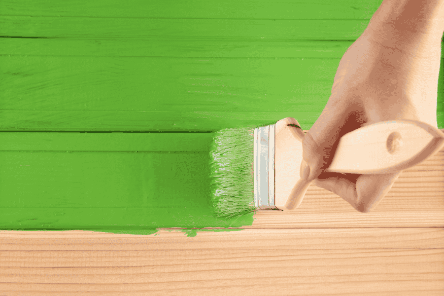 Mão pintando madeira com tinta verde usando pincel largo