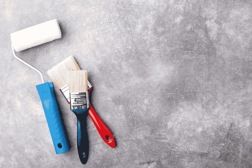 Conjunto de pincéis e rolo de pintura sobre superfície de concreto