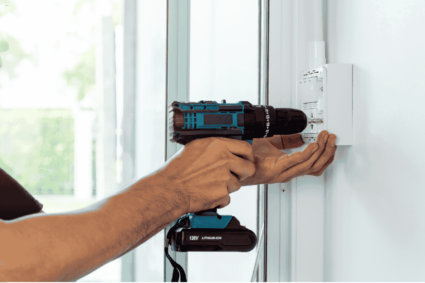 Homem utilizando furadeira para fixar novo interruptor na parede.