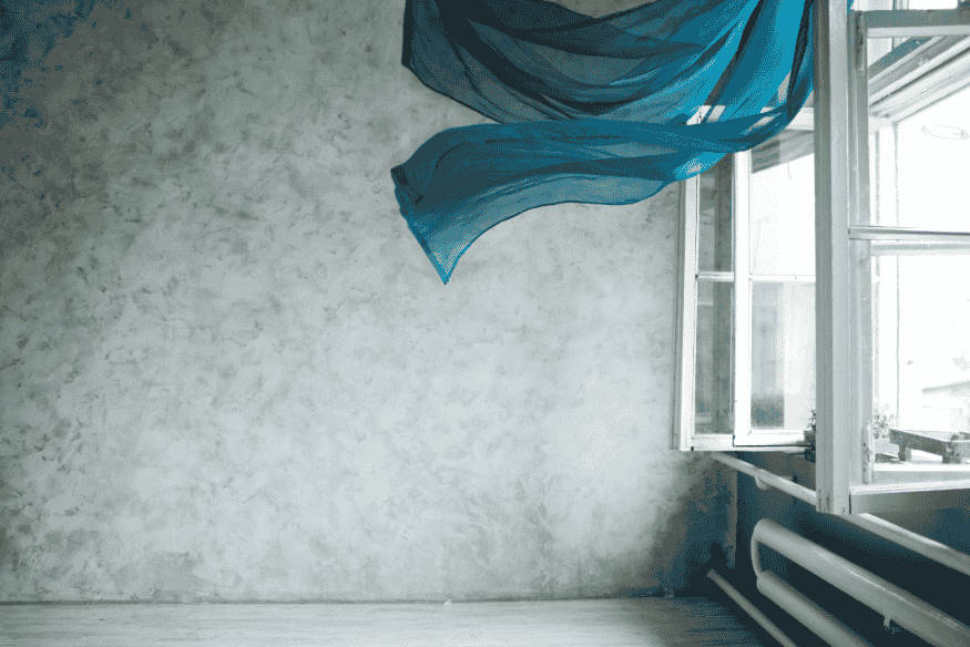 Quarto minimalista com parede de cimento queimado e cortina azul esvoaçante para ventilação natural